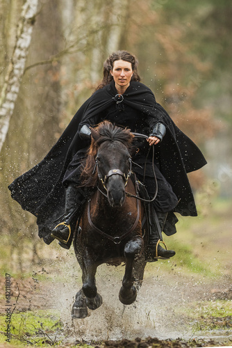 Beautiful woman in historical costume riding fast on horseback over puddles