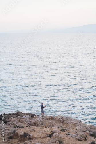 Rybak stojący na krawędzi skały na tle morza