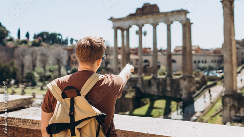 Young man tourist in sunglasses resting at Roman Forum. Historical imperial Foro Romano from panoramic point of view, Italy. Concept of travel, tourism and vacation in city. photo