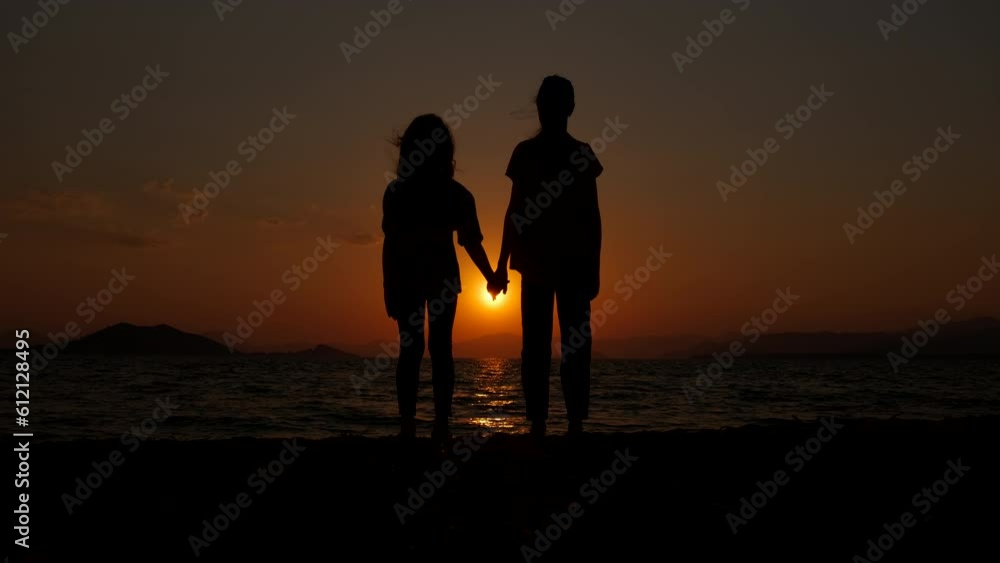 Silhouette of children at sunset. Little girls hold hands against the backdrop of a sea sunset. Silhouette of children at sunset. Little girls hold hands against the backdrop of a sea sunset.