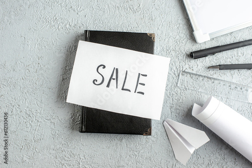 Above view of SALE writing on white sheet on black notebook pens ruler desk blank on gray sand background photo