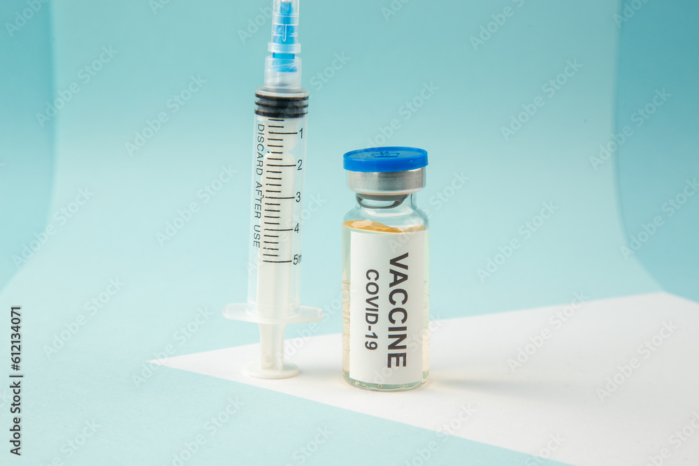 Close up view of covid- vaccine in medical ampoule and empty disposable syringe on blue background Close up view of covid- vaccine in medical ampoule and empty disposable syringe on blue background