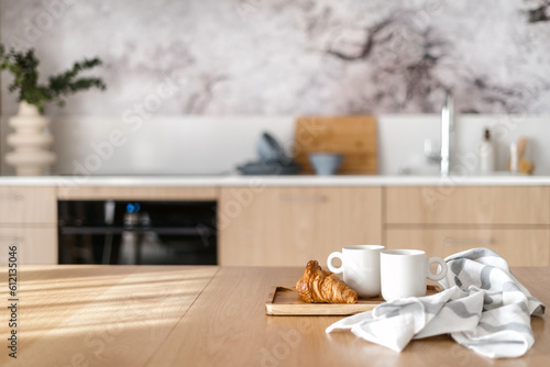 Photo wooden table with mugs of tea and fresh pastry in modern kitchen