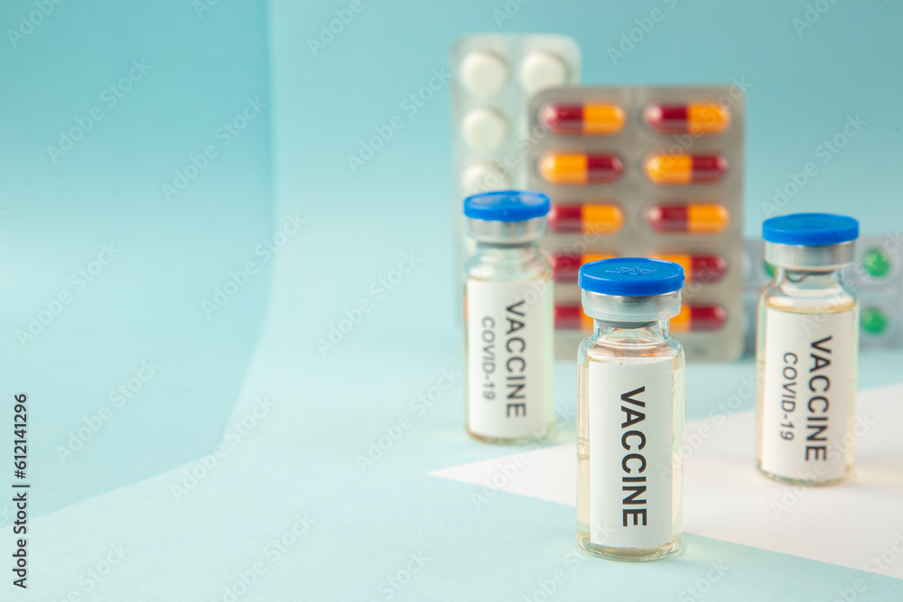 Front close view of vaccine in medical ampoules packed pills and capsules for treatment on the left side on pastel blue background Front close view of vaccine in medical ampoules packed pills and capsules for treatment on the left side on pastel blue background