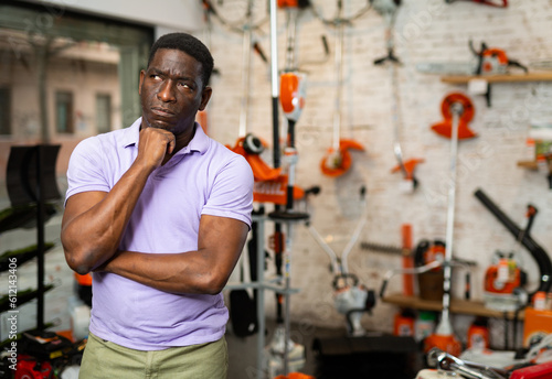 Thoughtful African-american man standing in salesroom of gardening tools store.