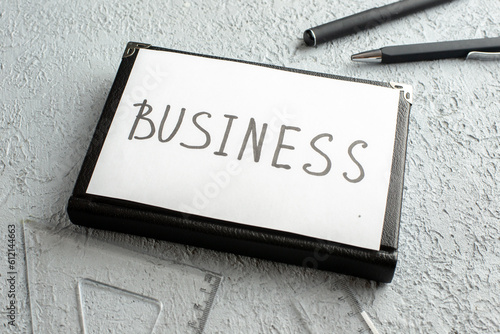 Front view of BUSINESS writing on white sheet on new black closed notebook ruler pens on gray sand background photo