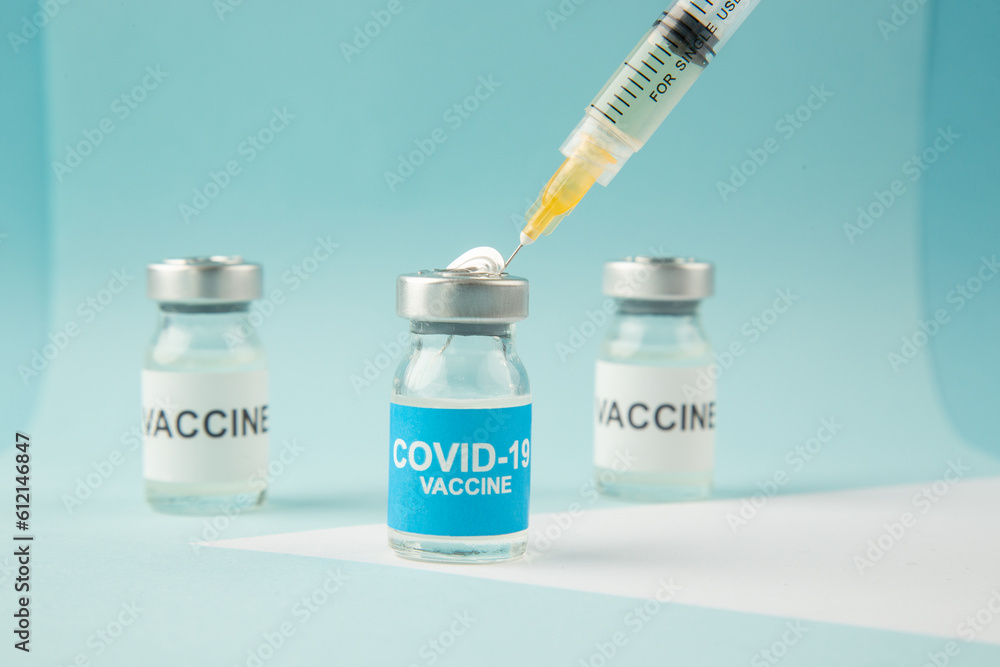 Front view of hand vaccine ampoules and syringe on pastel blue and white background with free space Front view of hand vaccine ampoules and syringe on pastel blue and white background with free space