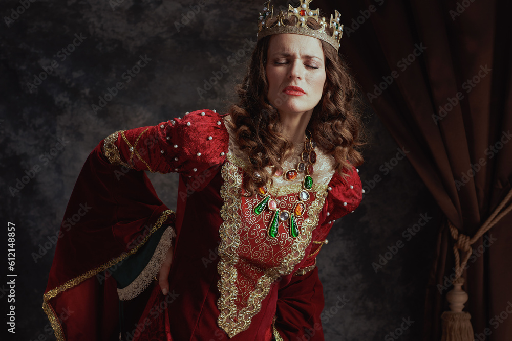 tired medieval queen in red dress with crown having backache