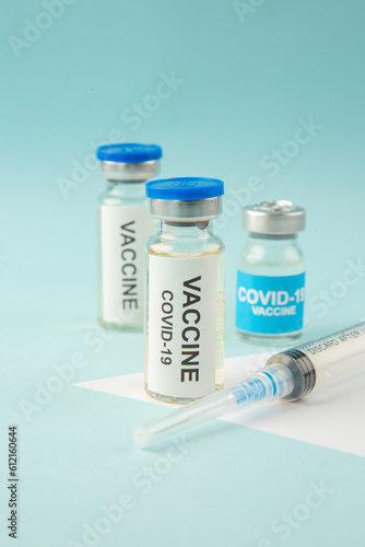 Side view of COVID- vaccine ampoules and disposable syringe on pastel blue and white background