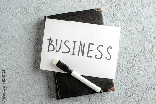 Top view of BUSINESS writing on white sheet and marker on new black closed notebook on gray sand background photo