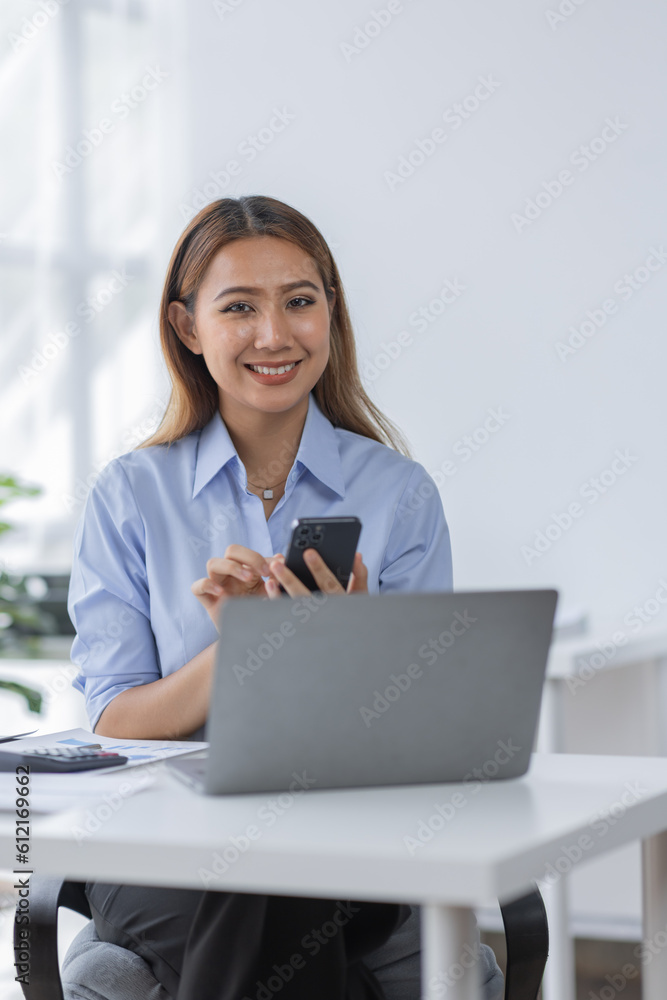 Smile business Asian woman freelancer is working her job on a laptop computer in a modern office. Do on phone accounting analysis report real estate investment data, Financial and tax systems concept.
