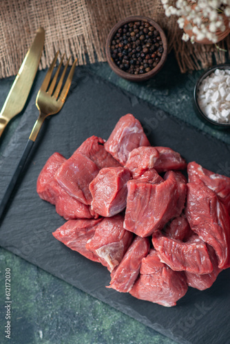 Top view of fresh raw chopped meats on wooden board cutlery set spices on dark background photo