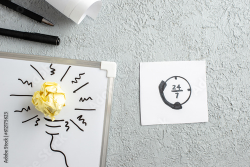 Top view of sheet with call line drawing incompletely drawn thing and crushed wrapped paper on white desk on gray sand background photo