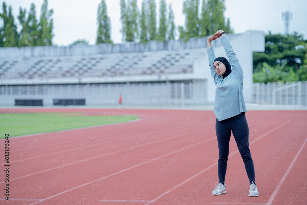 A young asian Muslim woman wearing a black hijab is exercising and running at an outdoor stadium in the morning. Modern Muslim woman concept,  Muslim woman sport concept, Islam