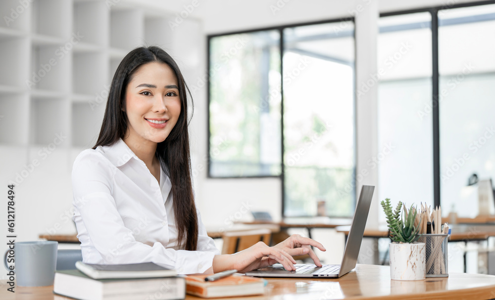 Charming Asian businesswoman working with a laptop at the office. Looking at camera. Charming Asian businesswoman working with a laptop at the office. Looking at camera.