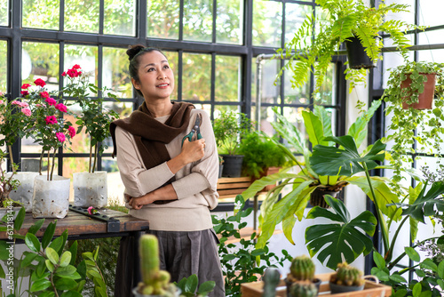 Happy gardener senior old eldery woman looking at young plant watering and gardening with potted plants taking care small tree in garden at home.Retirement concept