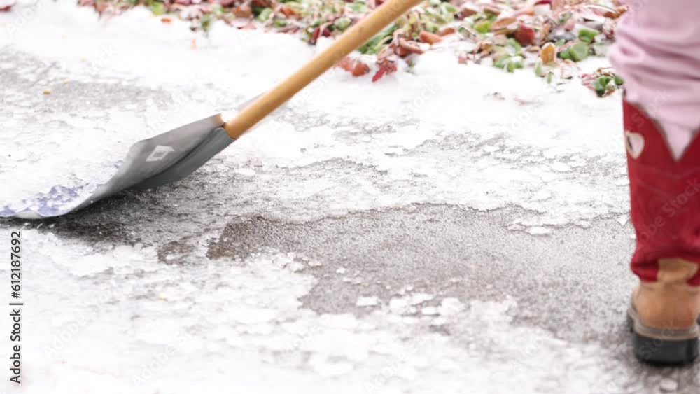 Child in cowboy boots shovels ice off a sidewalk in winter in slow motion. Child in cowboy boots shovels ice off a sidewalk in winter in slow motion.