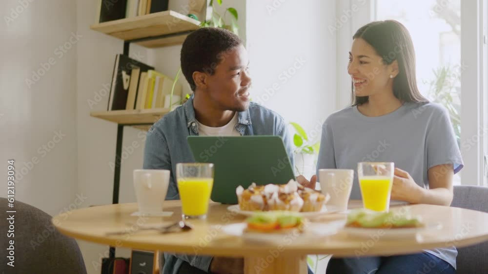 Multiethnic couple using a laptop and smiling during breakfast Multiethnic couple using a laptop and smiling during breakfast