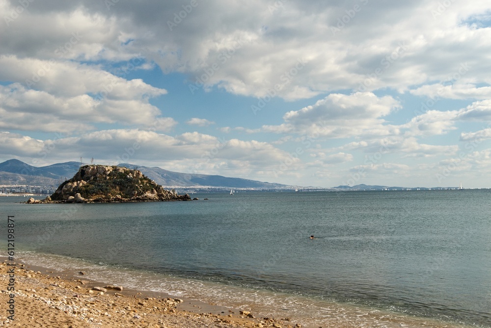 Beautiful photo of calm Votsalakia beach (Riviera Beach) without people with small island in the background, Pireaus Beautiful photo of calm Votsalakia beach (Riviera Beach) without people with small island in the background, Pireaus