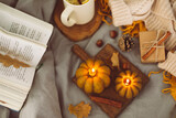 Top view on cozy mood composition with book, pumpkin candles, cup with hot tea and autumn decoration