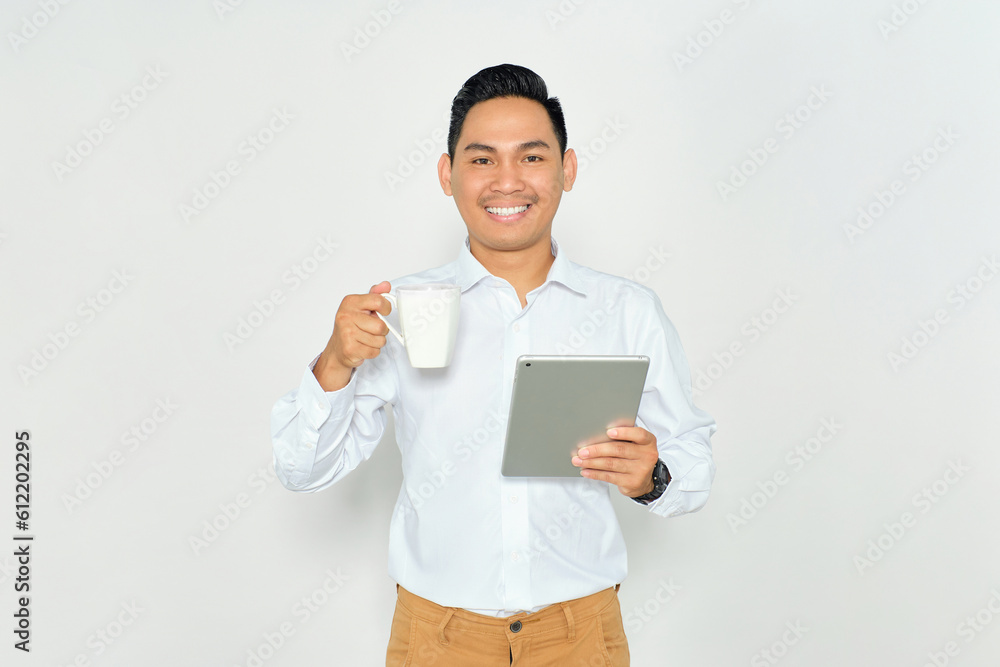 Portrait of smiling young Asian man in formal wear using digital tablet and holding cup of coffee, looking at camera with happy expression isolated on white background Portrait of smiling young Asian man in formal wear using digital tablet and holding cup of coffee, looking at camera with happy expression isolated on white background