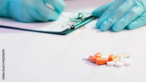 Medical prescription. Drug therapy. Doctor hands in blue protective rubber gloves filling in form on white table with pile of pills empty space.