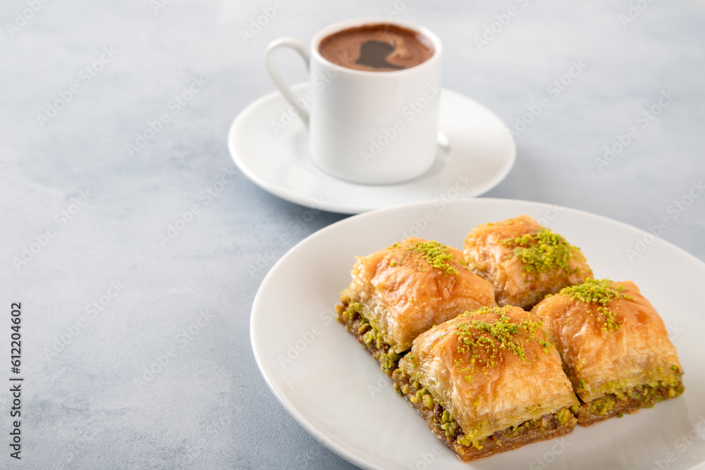 Pistachio baklava on a white plate with Turkish coffee.A plate of traditional baklava on light blue background Pistachio baklava on a white plate with Turkish coffee.A plate of traditional baklava on light blue background