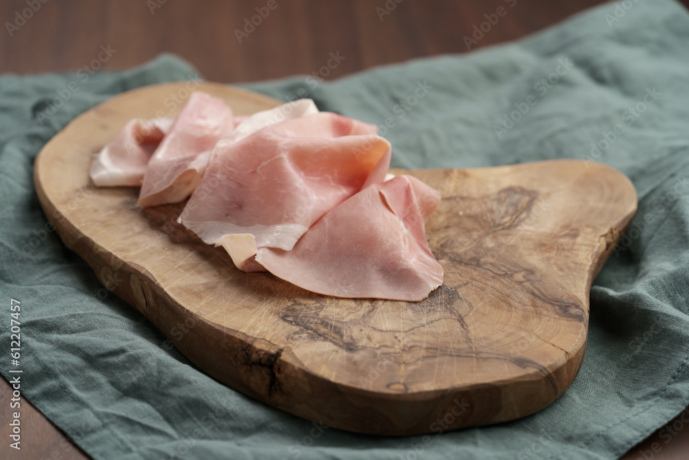 Thin slices of prosciutto cotto on olive wood board