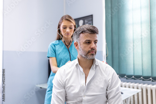 A female doctor at the clinic performs auscultation of the lungs of a patient with symptoms of coronavirus or pneumonia. He is coughing the doctor listens to the wheezing in the lungs