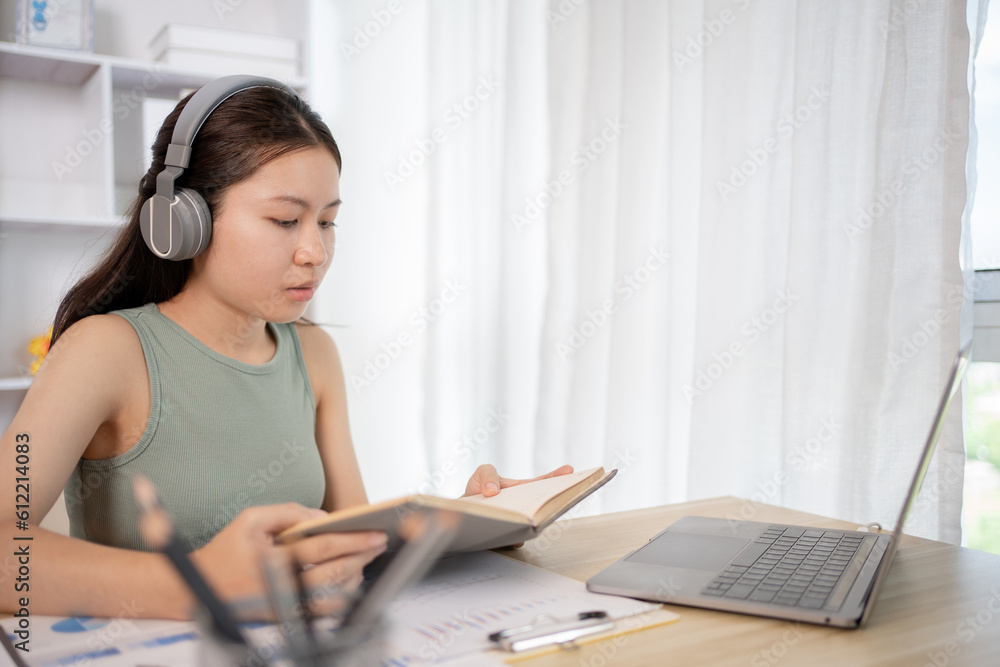 Obraz premium Young female student reading a book in a private office, Self study, Textbooks from books, Find out more, In the office there is a computer or laptop placed on the table, Study.