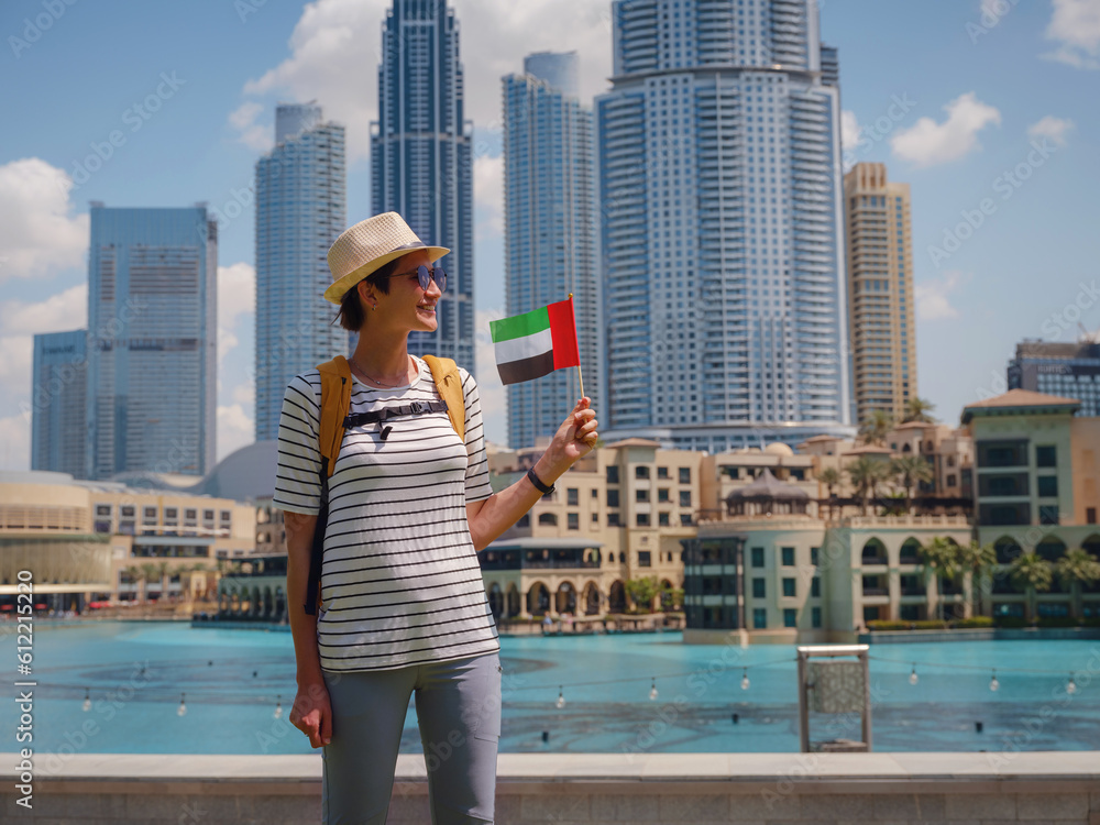 Enjoying travel in United Arabian Emirates. Young woman with yellow backpack with the flag of the United Arab Emirates walking on Dubai Downtown in sunny summer day.