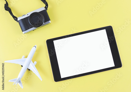 flat lay of digital tablet with blank white screen, airplane model and digital camera isolated on yellow background. travel planning concept.