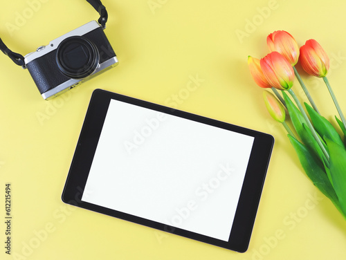 Fototapeta Naklejka Na Ścianę i Meble -  flat lay of digital tablet with blank white screen, tuip flowers  and digital camera isolated on yellow background.