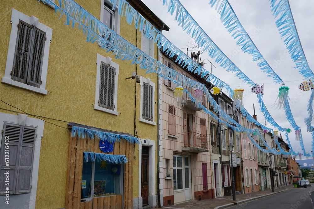 blue garland and jellyfish decorations above the street in a small village by colorful buildings in the mountains of the southern Alps, France