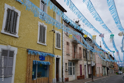 Fototapeta Naklejka Na Ścianę i Meble -  blue garland and jellyfish decorations above the street in a small village by colorful buildings in the mountains of the southern Alps, France