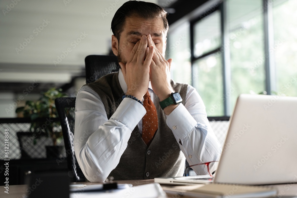 Feeling exhausted. Frustrated middle-aged beard man massaging his nose and keeping eyes closed while sitting at his working place in office. Feeling exhausted. Frustrated middle-aged beard man massaging his nose and keeping eyes closed while sitting at his working place in office.