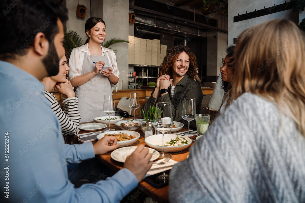 Beautiful waitress serving group of cheerful friends in restaurant Beautiful waitress serving group of cheerful friends in restaurant