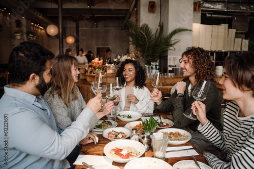 Group of joyful friends talking and drinking wine while dining in restaurant
