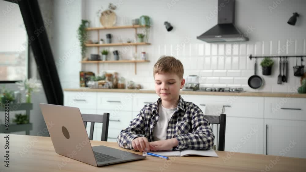 School Boy Studying Online Using Laptop at Home. Kid writing in notebook and listening to online teacher. Distance education. School Boy Studying Online Using Laptop at Home. Kid writing in notebook and listening to online teacher. Distance education.