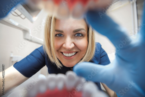 Close-up smiling female dentist examining teeth in clinic in first person. View through the mouth dental checkup.