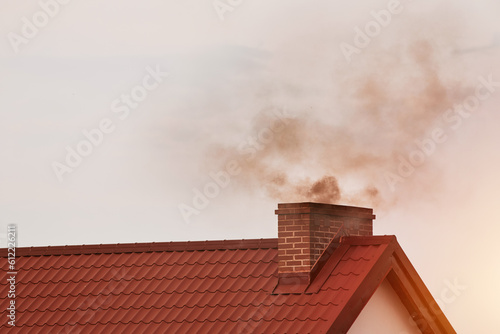 Dark smoke comes out of the chimney of a modern house in winter. Heating with solid fuel. The concept of environmental pollution