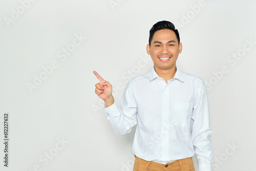 Portrait of smiling young Asian man in formal wear pointing fingers aside at copy space, presents something isolated on white background