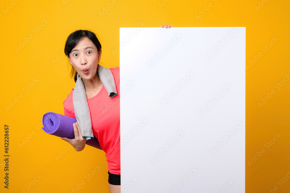 young asian sports fitness woman happy smile wearing pink sportswear standing behind the white blank banner or empty space advertisement board against yellow background. wellbeing lifestyle concept. young asian sports fitness woman happy smile wearing pink sportswear standing behind the white blank banner or empty space advertisement board against yellow background. wellbeing lifestyle concept.