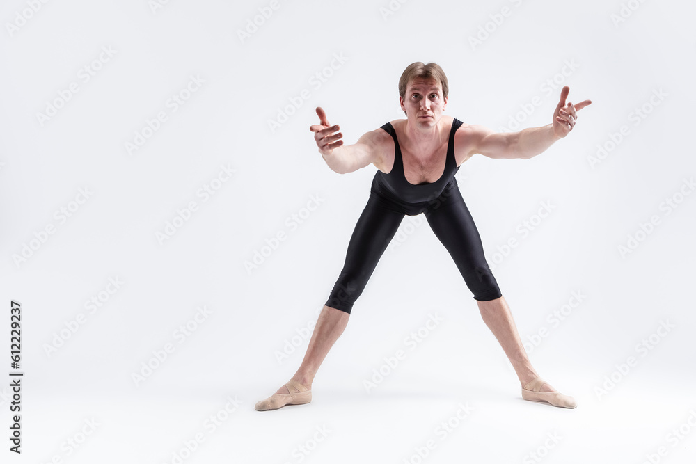 Caucasian Relaxed Ballerino Dancer Sitting While Practising Waist and Body Stretching Exercices With Lifted hands In Black Sportive Tights in Studio. Caucasian Relaxed Ballerino Dancer Sitting While Practising Waist and Body Stretching Exercices With Lifted hands In Black Sportive Tights in Studio.