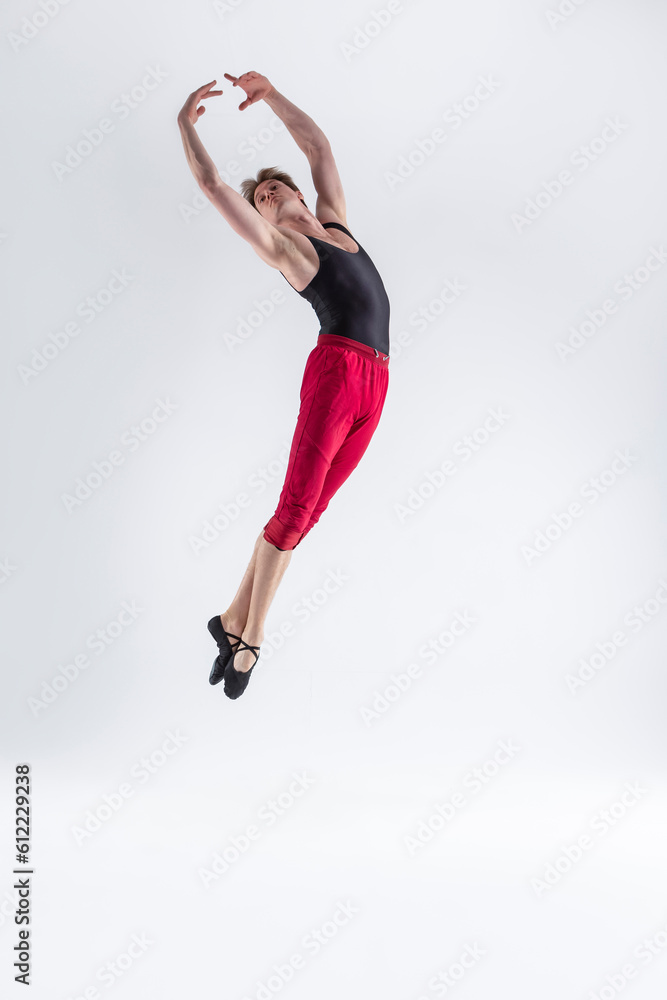 Contemporary Ballet of Young Flexible Athletic Man Posing in Red Tights in Flying Dance Pose With Hands Lifted and Connected in Studio on White.
