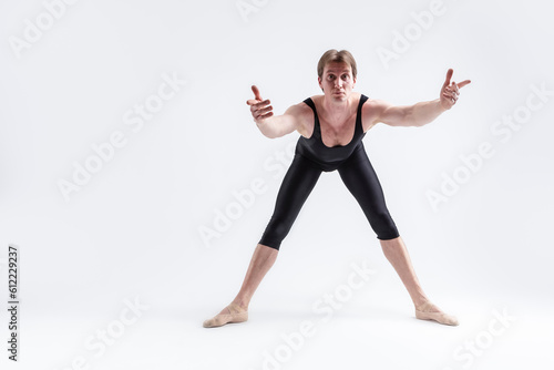 Caucasian Relaxed Ballerino Dancer Sitting While Practising Waist and Body Stretching Exercices With Lifted hands In Black Sportive Tights in Studio.