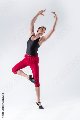 Contemporary Ballet of Flexible Athletic Man Posing in Red Tights in Ballanced Dance Pose With Hands Lifted in Studio on White.