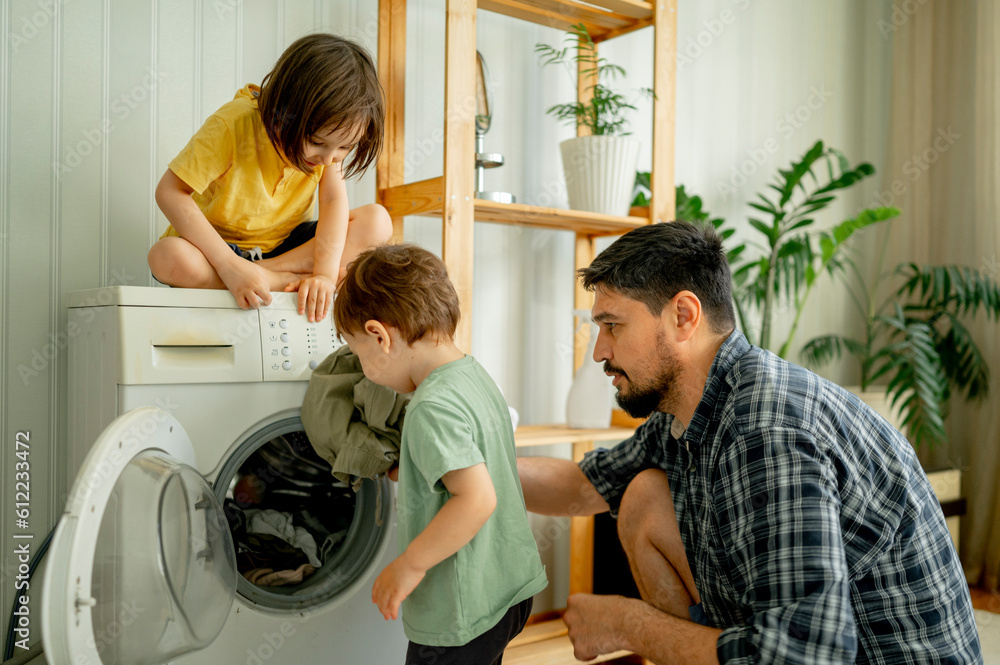 Father with children helping washing clothes in machine at home Father with children helping washing clothes in machine at home