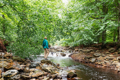 Senior man standing on rock by river in forest