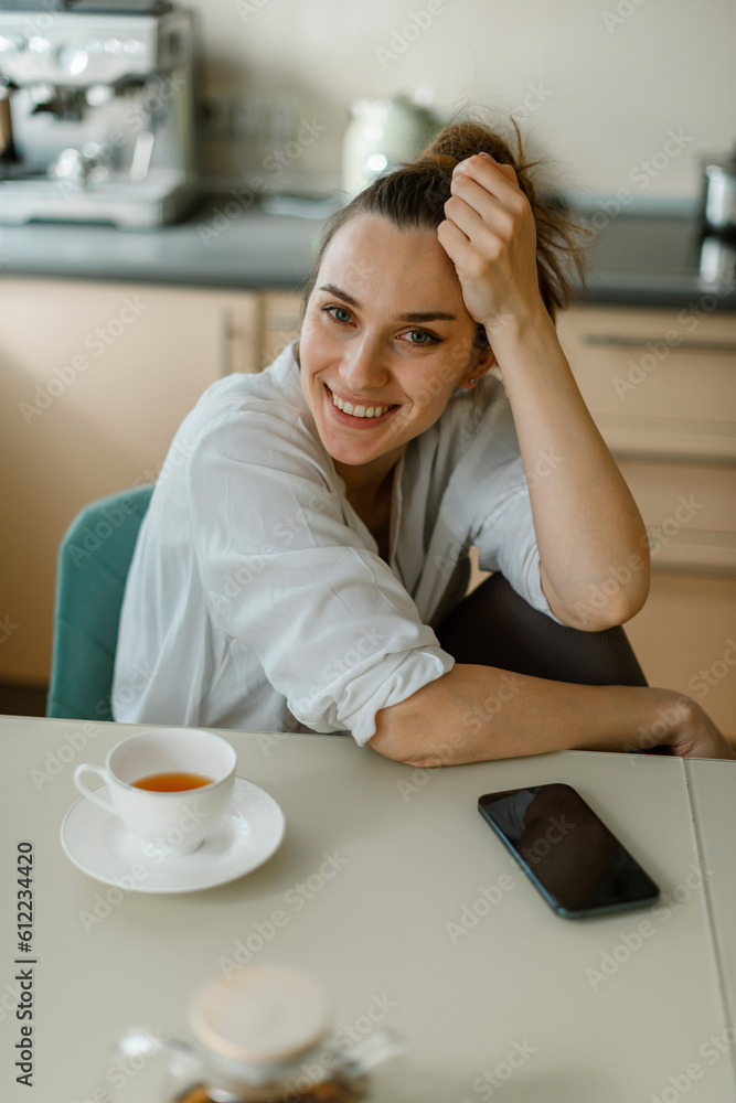 Smiling woman sitting on table with smart phone and tea Smiling woman sitting on table with smart phone and tea